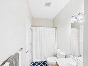 Apartments for rent in Limerick PA USA A bathroom with white walls, a shower with a white curtain, a toilet, a sink with a mirror, and a blue patterned rug.