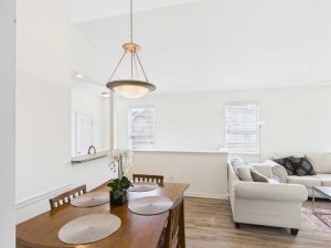 Apartments for rent in Limerick PA USA A dining table with four chairs and placemats is set near a living area with a light-colored sofa and windows in a bright, open room.