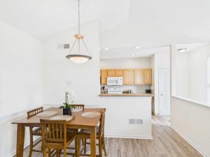 Apartments for rent in Limerick PA USA A small dining area with a wooden table and four chairs is set next to a kitchen with light wood cabinets and white appliances. A pendant light hangs above the table.