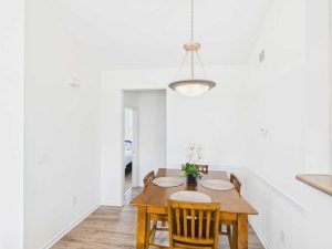 Apartments for rent in Limerick PA USA A wooden dining table with four chairs, set with placemats and a flower centerpiece, sits in a bright, white-walled room with a hanging light fixture above.