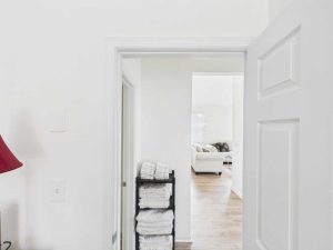 Apartments for rent in Limerick PA USA Open white door revealing a hallway with a black shelf stacked with white towels; in the background, a living room with a white sofa and sunlight coming through windows.