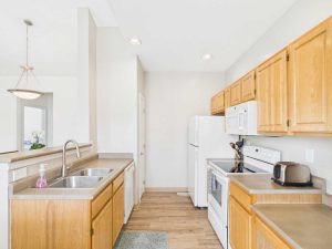 Apartments for rent in Limerick PA USA A tidy kitchen with light wood cabinets, white appliances, a double sink, toaster, and soap dispenser on the counter, and a hanging light fixture in the adjacent room.