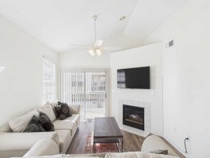 Apartments for rent in Limerick PA USA Bright living room with two beige sofas, a wooden coffee table, wall-mounted TV above a fireplace, and sliding glass doors letting in natural light.
