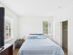 Apartments for rent in Limerick PA USA A bedroom with a neatly made bed, two windows, a nightstand with a lamp, an open closet door, and a TV in the foreground.