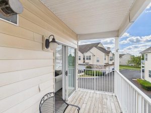 Apartments for rent in Limerick PA USA A small balcony with a metal chair, wooden floor, and white railing, overlooking a parking area and neighboring residential buildings under a partly cloudy sky.