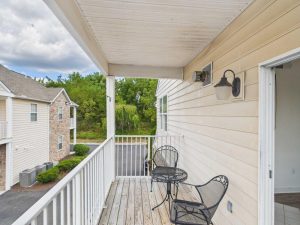 Apartments for rent in Limerick PA USA A small apartment balcony with two black metal chairs, a round table, and a white railing, overlooking a parking lot and neighboring buildings.