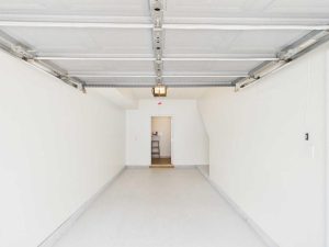 Apartments for rent in Limerick PA USA Empty, clean single-car garage with white walls and floor, garage door open, and a door at the far end leading into a house interior.