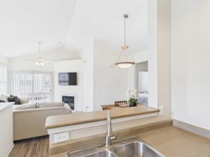 Apartments for rent in Limerick PA USA A kitchen sink and countertop overlook a living area with a beige sofa, fireplace, dining table, and large windows.