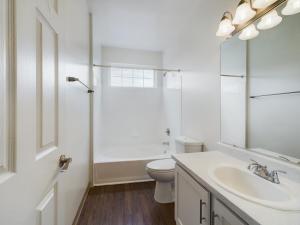 A white bathroom with wood floors and a sink that is perfect for capturing media content.